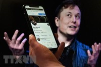 Tài khoản Twitter của tỷ phú Elon Musk trên màn hình điện thoại và ảnh chụp ông Musk (phía sau) tại một sự kiện ở Washington, DC, Mỹ ngày 14/4/2022. (Ảnh: AFP/TTXVN)