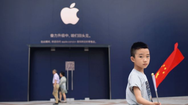 Một cậu bé cầm quốc kỳ Trung Quốc bên ngoài cửa hàng của Apple. (Ảnh: Getty).