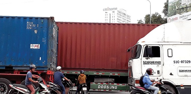 Bị xe container bịt kín lối đi, người dân phải luồn lách trước bánh xe “hung thần” để về nhà. Ảnh: Việt Dũng