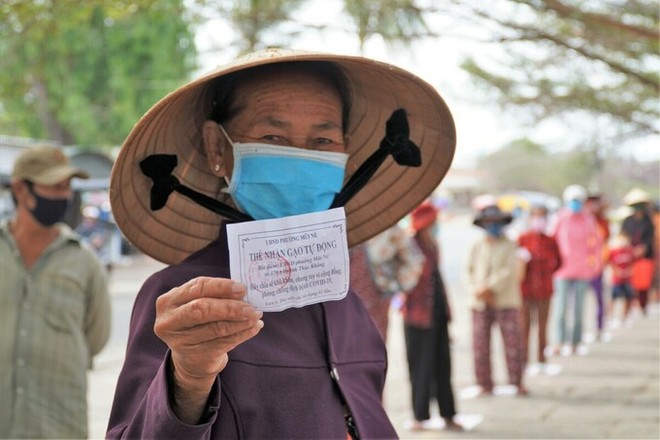 Bà Trần Thị Đảnh, 65 tuổi, cầm phiếu, đứng đầu hàng chuẩn bị vào bấm máy nhận gạo trước trụ sở phường Mũi Né.