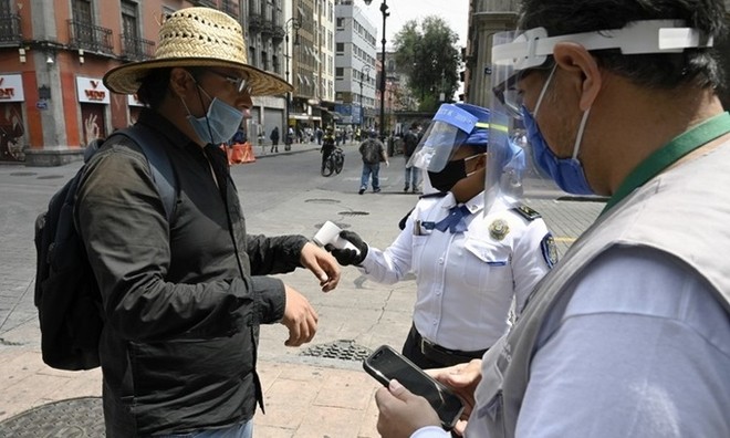 Cảnh sát và nhân viên y tế kiểm tra thân nhiệt của một người qua đường tại thủ đô Mexico City, Mexico hôm 6/7. Ảnh: AFP.