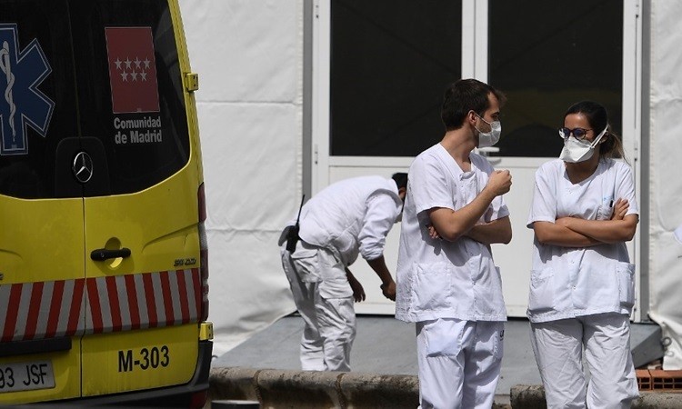Hai nhân viên y tế trò chuyện cạnh xe cứu thương bên ngoài bệnh viện La Paz ở Madrid hôm 23/3. Ảnh: AFP.