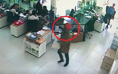 Tên cướp (khoanh tròn đỏ) cầm bao tải trắng tiến thẳng vào quầy gom tiền. Ảnh: Cắt từ camera.