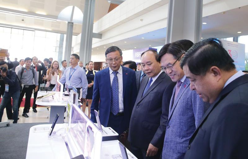 Thủ tướng Chính phủ Nguyễn Xuân Phúc (thứ ba, từ phải qua), Bộ trưởng Bộ Kế hoạch và Đầu tư Nguyễn Chí Dũng (ngoài cùng, bên phải) thăm gian hàng của Sam sung tại triển lãm tổ chức nhân Hội nghị 30 năm thu hút FDI.