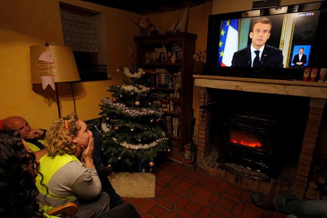 Người biểu tình “Áo ghi-lê vàng” nghe bài phát biểu của Tổng thống Pháp Emmanuel Macron trên truyền hình tại Gaillon hôm 10-12 Ảnh: REUTERS.