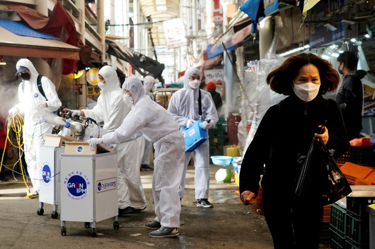 Một người phụ nữ Hàn Quốc đeo khẩu trang khi các nhân viên của công ty diệt khuẩn làm việc tại khu chợ truyền thống tại Seoul hôm 26/2. Ảnh: Reuters.