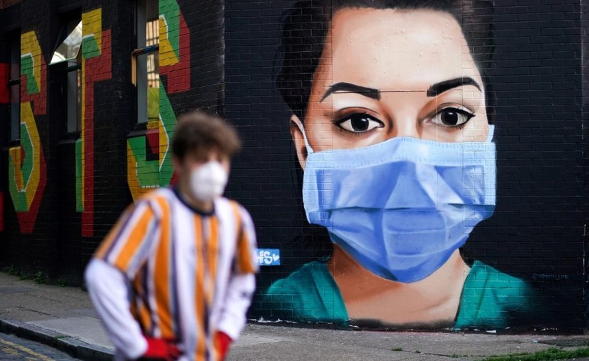 Một người đàn ông đi qua một bức vẽ mô tả một y tá đeo khẩu trang ở London, Anh. (Ảnh: Reuters).