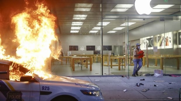 Một người chạy khỏi Apple Store tại Philadelphia trong khi một chiếc xe cảnh sát đỗ phía trước cửa hàng bị đốt cháy, ngày 30/5/2020. (Nguồn: AP).