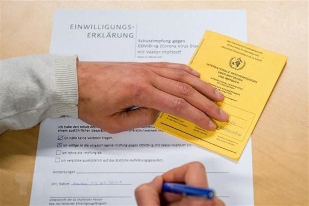 Người dân điền thông tin vào bản khai bên thẻ Chứng nhận tiêm vaccine ngừa COVID-19 do Tổ chức Y tế Thế giới (WHO) cấp phép, tại điểm tiêm chủng ở Halle/Saale, miền Đông Đức. (Ảnh minh họa: AFP/TTXVN).