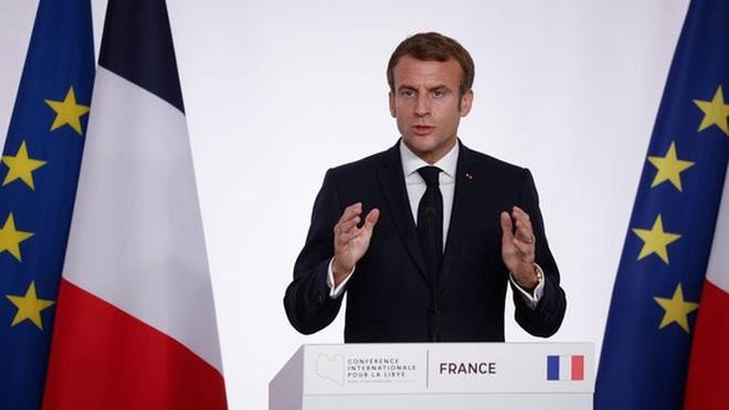 Tổng thống Pháp Emmanuel Macron bên cạnh quốc kỳ Pháp đã có thay đổi màu lam sáng thành lam đậm (Ảnh: AP).