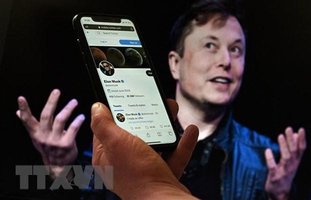 Tài khoản Twitter của tỷ phú Elon Musk trên màn hình điện thoại và ảnh chụp ông Musk (phía sau) tại một sự kiện ở Washington, DC, Mỹ ngày 14/4/2022. (Ảnh: AFP/TTXVN)