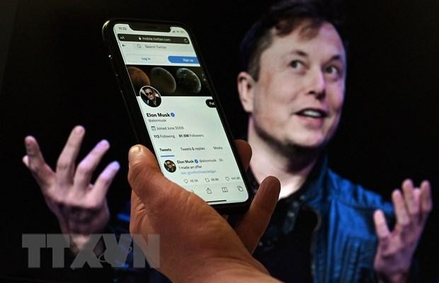 Tài khoản Twitter của tỷ phú Elon Musk trên màn hình điện thoại và ảnh chụp ông Musk (phía sau) tại một sự kiện ở Washington, DC, Mỹ ngày 14/4/2022. (Ảnh: AFP/TTXVN).