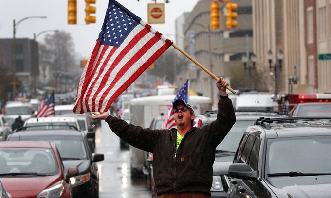 Người đàn ông cầm cờ Mỹ biểu tình phản đối phong tỏa vì Covid-19 tại thành phố Lansing, bang Michigan, hồi tháng 4. Ảnh: AP.