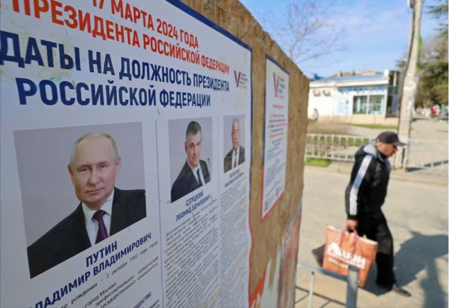 Một người đàn ông đi ngang qua bảng thông tin có chân dung của các ứng cử viên tổng thống Nga trong cuộc bầu cử sắp tới ở Yevpatoriya, Crimea ngày 8/3/2024. Ảnh: REUTERS